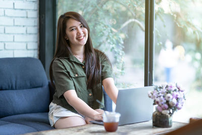 Portrait of young woman using mobile phone while sitting at home