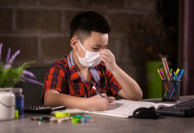 Happy boy studying with face mask on table at home