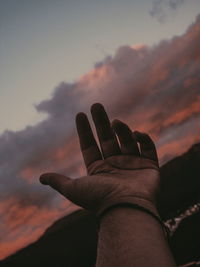 Cropped hand against sky during sunset