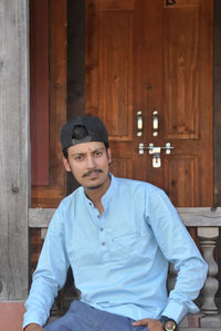 A good looking young guy with wearing cap backwards, looking at camera while sitting in temple 