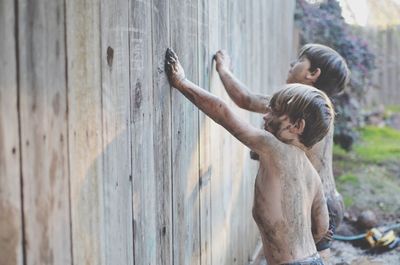 Dirty shirtless boys touching wooden wall