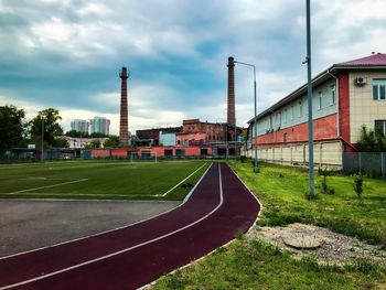 Street amidst field and buildings against sky