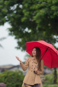 Young woman with red umbrella standing against tree