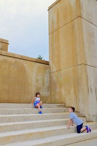 Siblings playing on steps against wall