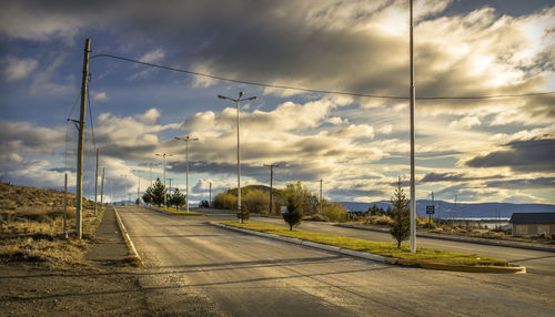 Road amidst field against cloudy sky