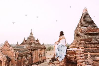 Rear view of woman sitting at temple against clear sky