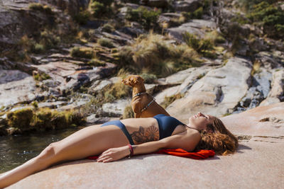 Woman wearing bikini resting on rock with dog in forest at la pedriza, madrid, spain