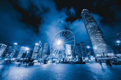 Illuminated ferris wheel against buildings at night