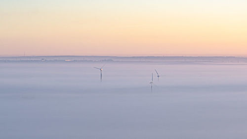 Windmills during foggy weather against orange sky