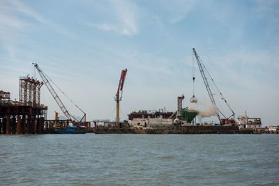 Cranes at commercial dock against sky