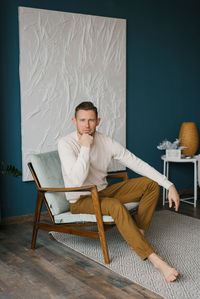 Young man sits lama in a cozy chair and looks at the camera person