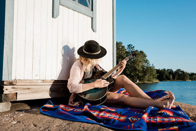 Woman sat on a rock at the beach playing the guitar on a sunny day