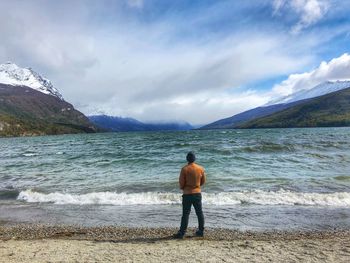 Rear view of man standing at beach against sky