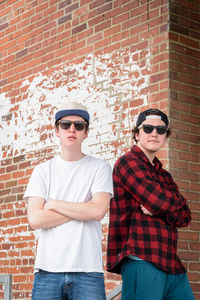 Portrait of young friends standing against brick wall