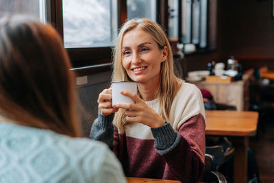 Portrait of an attractive blonde chatting with a friend while sitting in a cozy warm cafe.