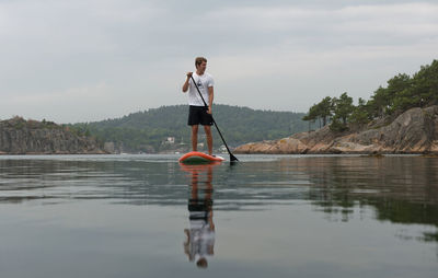 Man paddleboarding in lake against sky