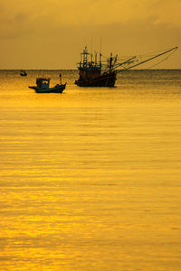 Fishing boats in sea against sunset sky