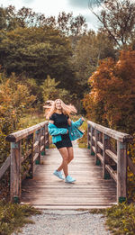 Portrait of happy teenage girl walking on footbridge in forest