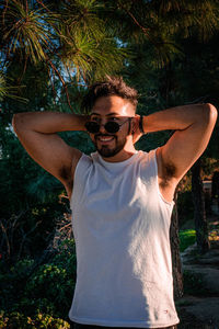 Young man wearing sunglasses standing by tree
