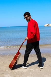 Full length of young man standing at beach against clear sky