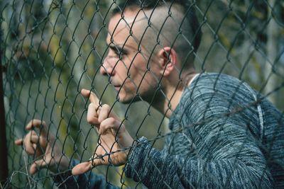 Young man looking through chainlink fence