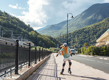 Young woman in protective equipment riding on roller skates along embankment , summer roller skating