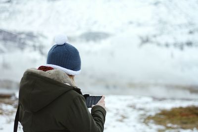 Rear view of person using phone on snow covered field