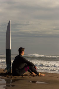 Man sitting on beach looking at sea against sky