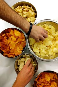 Cropped hands of people picking chips from container on table