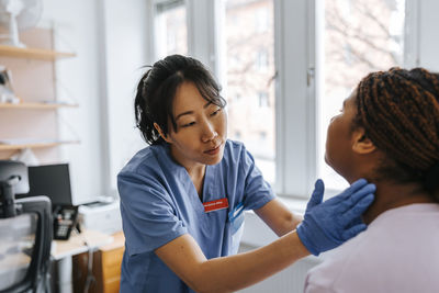 Female medical expert checking lymph nodes of young patient in examination room at hospital