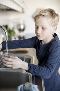 Boy filling water in glass from faucet in kitchen