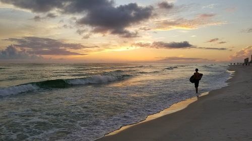 Man walking on beach against sky during sunset