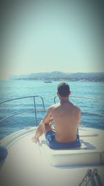 Rear view of shirtless man in boat sailing on sea against clear sky