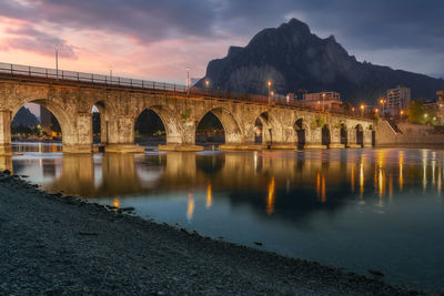 Bridge over river against sky at sunset