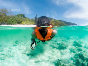 Man with smart phone snorkeling in sea against sky