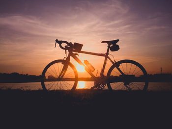 Silhouette bicycle on field against sky during sunset