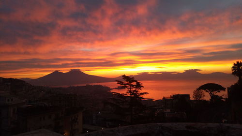 Silhouette buildings and mountains against romantic sky at sunset