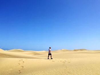 Man walking on desert against clear blue sky