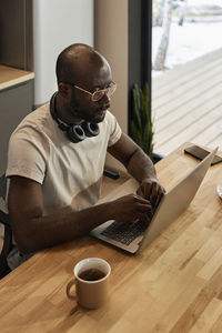 Man using laptop on table by tea cup at home