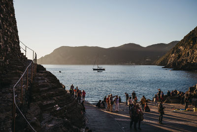 People on sailboats by sea against clear sky