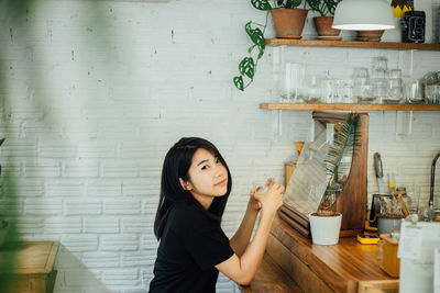 Side view portrait of woman having drink while sitting at table in cafe