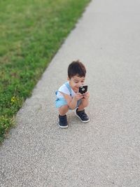 High angle view of cute boy using mobile phone while crouching on road