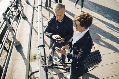 High angle view of senior couple using mobile phones while standing on sidewalk in city