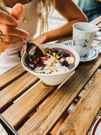 Midsection of woman eating breakfast, acai bowl with fruits, healthy eating in restaurant.