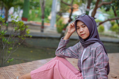 Portrait of young woman looking away while sitting outdoors