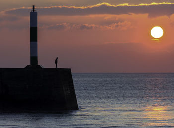 Silhouette of lighthouse at seaside during sunset