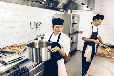 Kvinnlig kock bär på gryta i restaurangkök