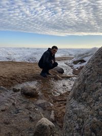Side view of man on rocks at beach against sky
