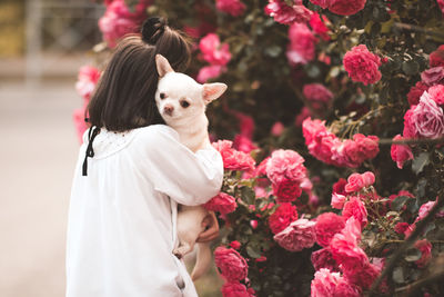 Kid girl 4-5 year old holding puppy pet standing over flower at background close up. childhood