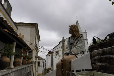 Low angle view of woman sitting against building and sky